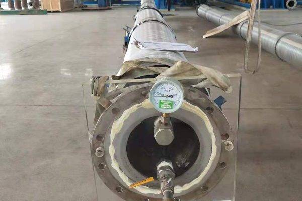 Submarine oil hose in Mozambique with flanged end and attached pressure gauge, lying on a workshop floor.